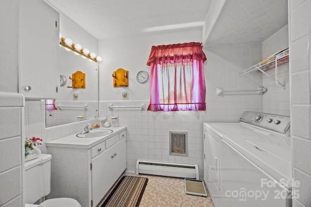 bathroom with washer and dryer, baseboard heating, vanity, toilet, and tile walls