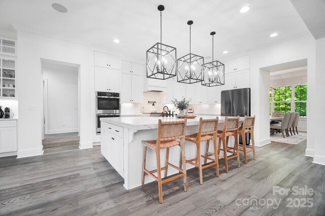 1005 Grand Oak Dr, Waxhaw, NC 28173 - kitchen with stainless steel double oven, wood finished floors, recessed lighting, a center island with sink, and white cabinets