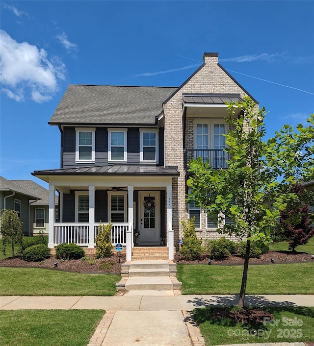 traditional home featuring covered porch, a standing seam roof, metal roof, roof with shingles, and a front lawn