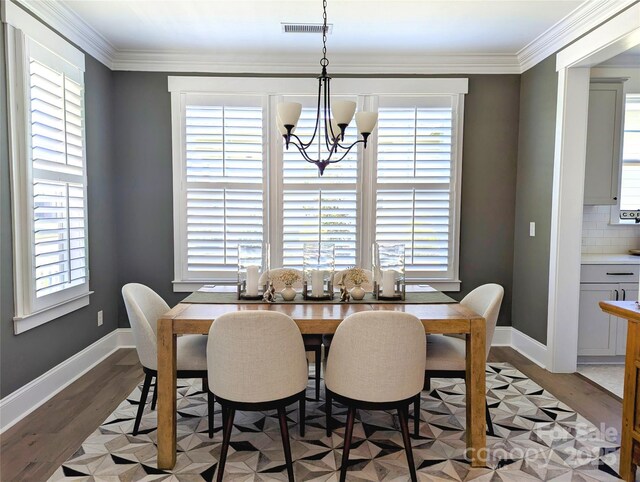 dining room with visible vents, ornamental molding, an inviting chandelier, light wood-style floors, and baseboards
