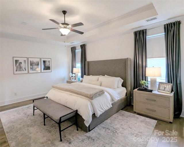 bedroom with visible vents, ornamental molding, wood finished floors, ceiling fan, and a tray ceiling