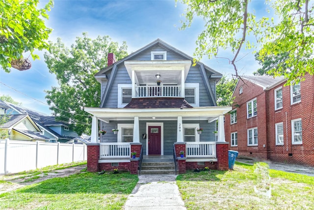 colonial inspired home with fence, a front yard, a chimney, a balcony, and covered porch
