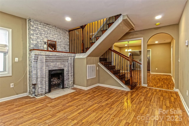 unfurnished living room featuring visible vents, a brick fireplace, wood finished floors, stairway, and baseboards