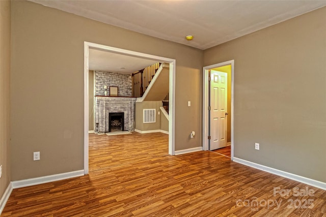 unfurnished living room with baseboards, visible vents, wood finished floors, and a fireplace