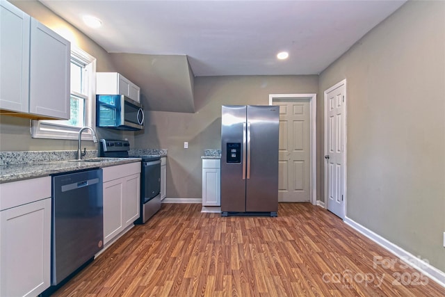 kitchen featuring light stone countertops, wood finished floors, a sink, baseboards, and stainless steel appliances