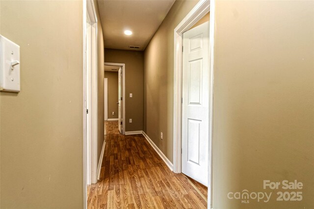 hallway with baseboards, visible vents, and wood finished floors