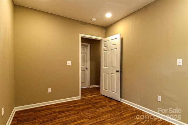 empty room with baseboards and dark wood-type flooring