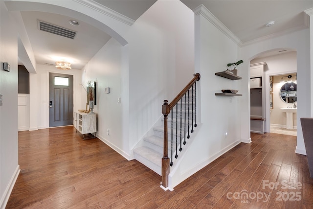entrance foyer featuring visible vents, arched walkways, crown molding, and wood finished floors