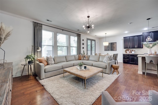 living area featuring dark wood-style floors, visible vents, ornamental molding, and an inviting chandelier
