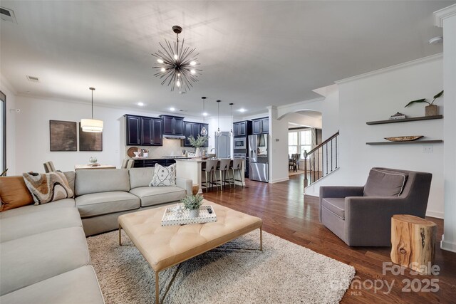 living area featuring arched walkways, ornamental molding, a chandelier, and dark wood-type flooring