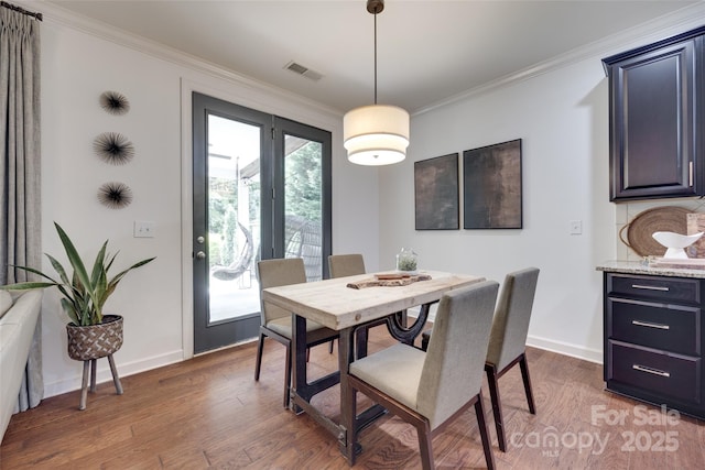 dining room with crown molding, baseboards, wood finished floors, and visible vents