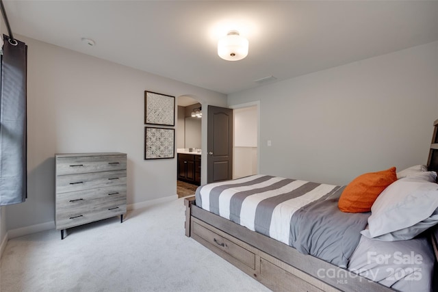 bedroom with baseboards, arched walkways, ensuite bathroom, and light carpet