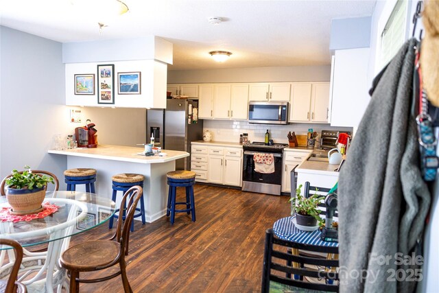 kitchen featuring a peninsula, dark wood-style floors, a kitchen bar, white cabinets, and stainless steel appliances