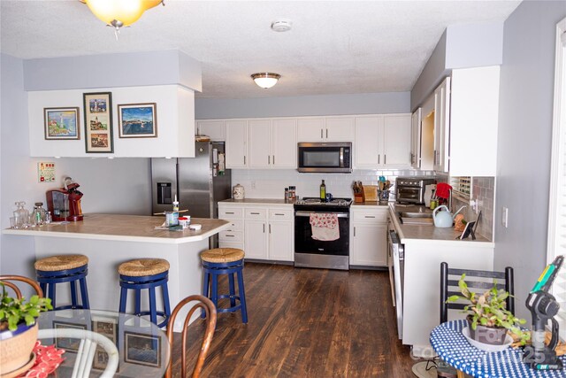 57 Gribble Rd, Franklin, NC 28734 - kitchen with stainless steel appliances, a breakfast bar, dark wood finished floors, a peninsula, and white cabinets