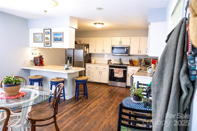 57 Gribble Rd, Franklin, NC 28734 - kitchen with stainless steel appliances, a peninsula, a kitchen breakfast bar, dark wood-style floors, and white cabinets