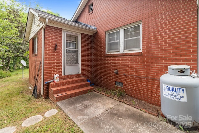 entrance to property featuring a yard, brick siding, and a patio area