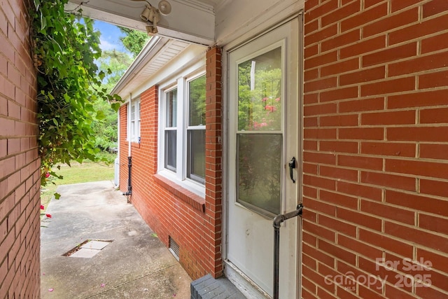 view of exterior entry with brick siding, crawl space, and visible vents