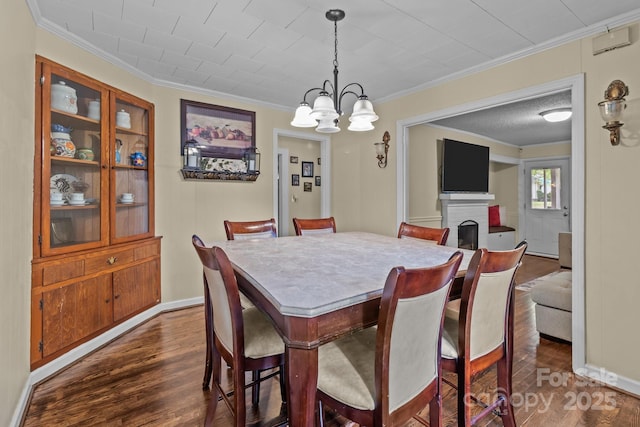 dining space with crown molding, a notable chandelier, a brick fireplace, and dark wood-type flooring