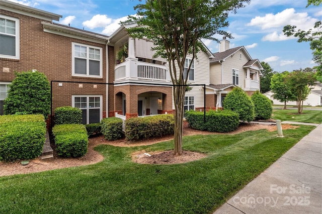 townhome / multi-family property featuring brick siding, a balcony, and a front lawn
