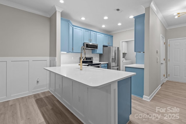 kitchen featuring blue cabinets, crown molding, appliances with stainless steel finishes, light wood-style floors, and washer and clothes dryer