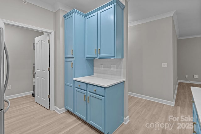 kitchen with blue cabinetry, crown molding, tasteful backsplash, light countertops, and light wood finished floors