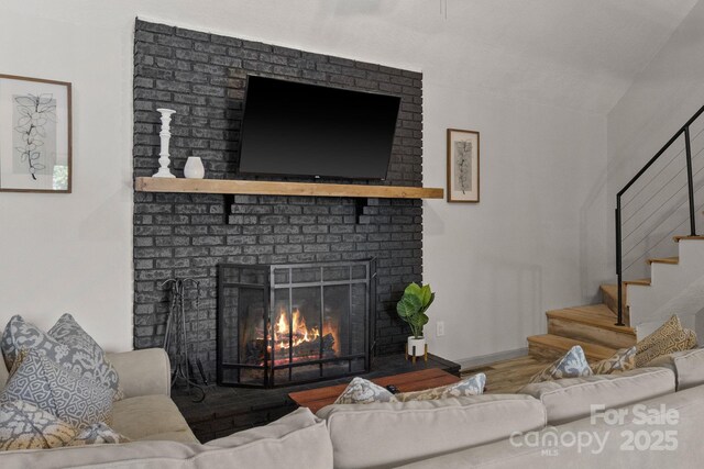 living room with stairs, a brick fireplace, and wood finished floors