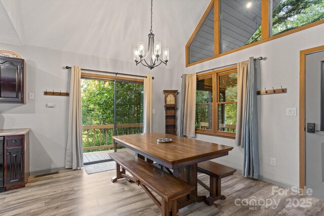 dining room featuring light wood-style floors, baseboards, high vaulted ceiling, and a notable chandelier
