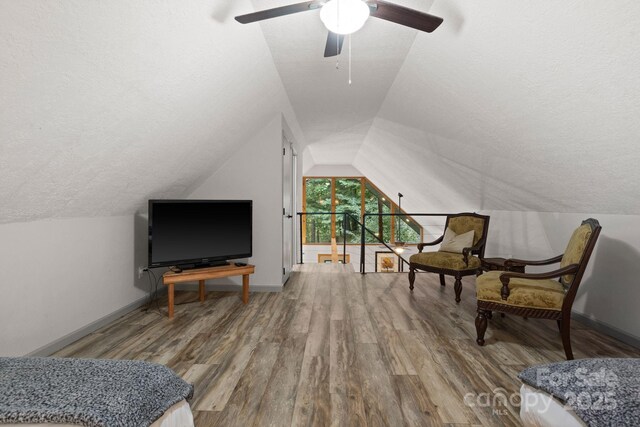 living area featuring ceiling fan, a textured ceiling, baseboards, wood finished floors, and vaulted ceiling