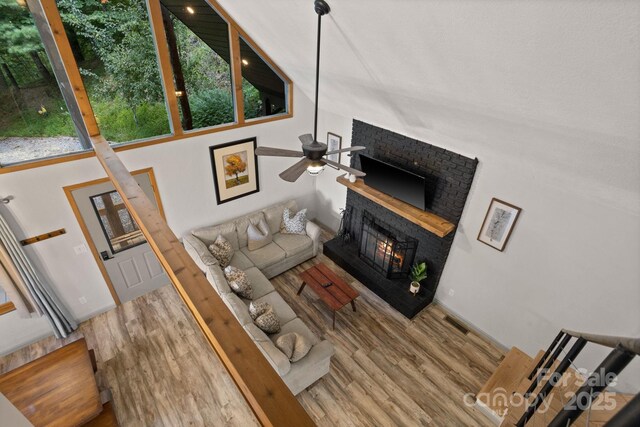 living area with a ceiling fan, a high ceiling, a brick fireplace, and wood finished floors