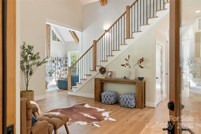 entrance foyer with stairs, high vaulted ceiling, baseboards, and wood finished floors