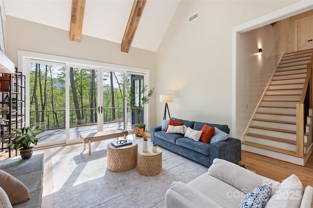 living area with beam ceiling, high vaulted ceiling, wood finished floors, visible vents, and stairway