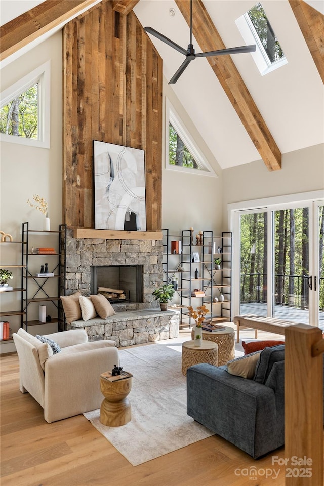 living room featuring beam ceiling, high vaulted ceiling, a stone fireplace, wood finished floors, and a skylight