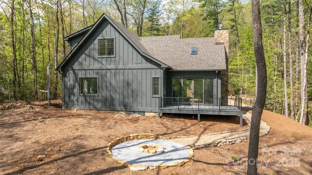 back of house with a chimney, board and batten siding, roof with shingles, and a deck