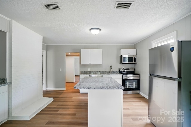 kitchen featuring visible vents, appliances with stainless steel finishes, a center island, white cabinets, and light wood-style floors