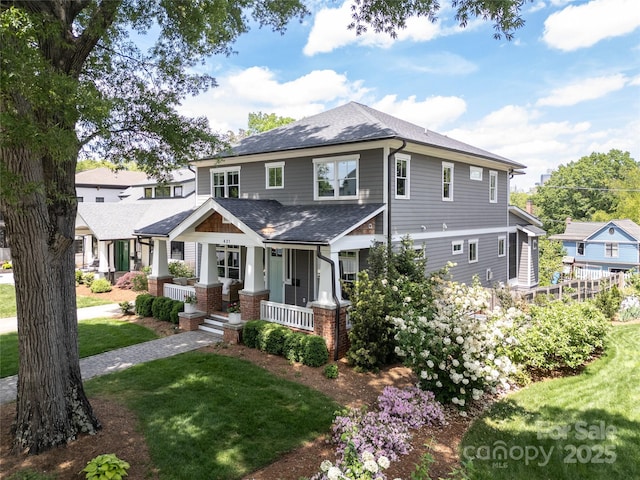 view of front of house with a front yard, a porch, brick siding, and roof with shingles