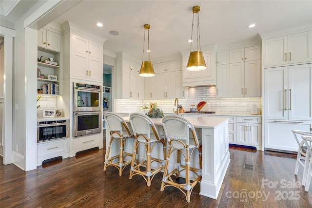 kitchen featuring dark wood-style flooring, a kitchen breakfast bar, light countertops, white cabinets, and appliances with stainless steel finishes