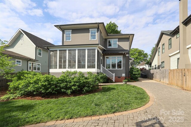 rear view of house featuring a sunroom, decorative driveway, fence, and a lawn
