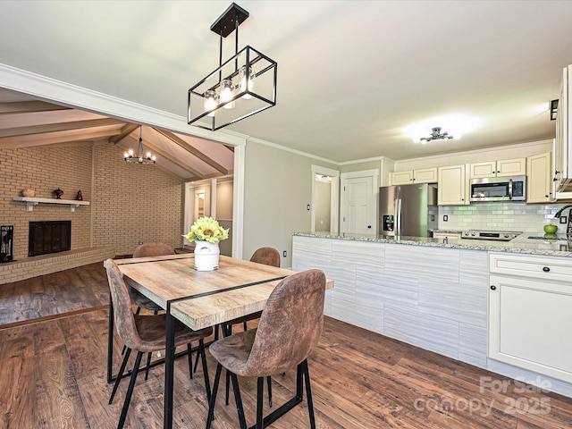 dining area featuring a brick fireplace, dark wood-style flooring, an inviting chandelier, and lofted ceiling with beams