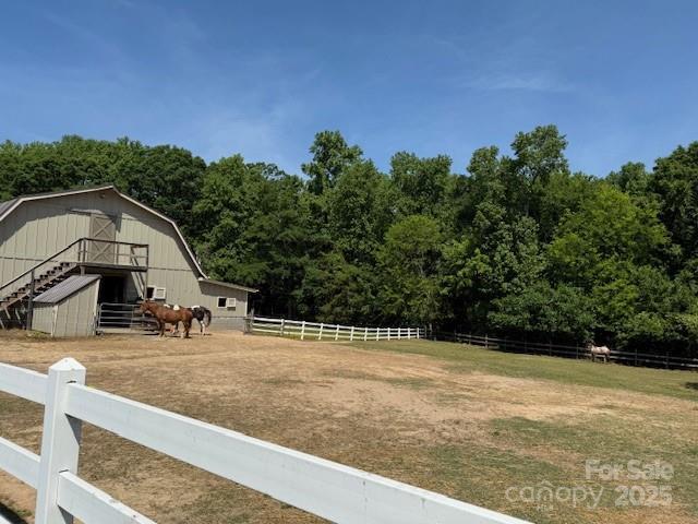 view of yard featuring fence, a barn, a view of trees, a rural view, and an outdoor structure