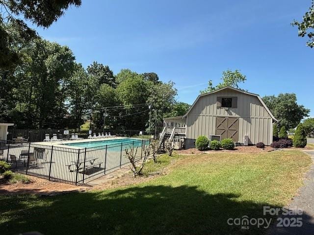 pool with fence, a barn, an outdoor structure, and a lawn