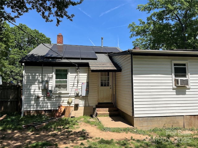 rear view of property featuring fence, cooling unit, a chimney, roof mounted solar panels, and entry steps