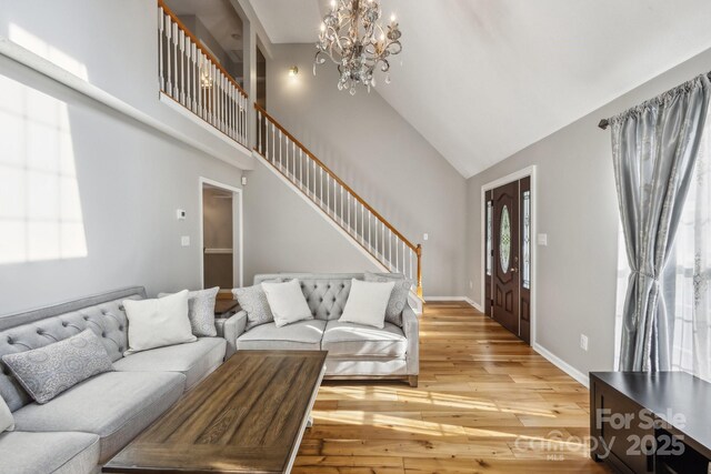 3223 Rheinwood Ct, Matthews, NC 28105 - living room with a chandelier, stairs, light wood-style floors, high vaulted ceiling, and baseboards