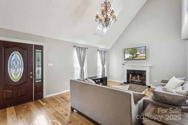 3223 Rheinwood Ct, Matthews, NC 28105 - living area featuring light wood-type flooring, high vaulted ceiling, baseboards, a tiled fireplace, and a chandelier
