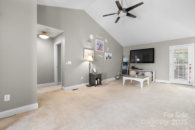 living area featuring ceiling fan, light colored carpet, a wood stove, high vaulted ceiling, and baseboards