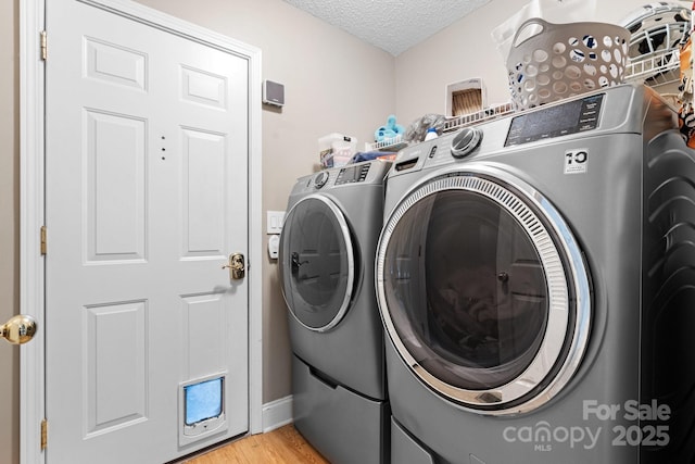 clothes washing area featuring laundry area, a textured ceiling, light wood finished floors, and washing machine and clothes dryer