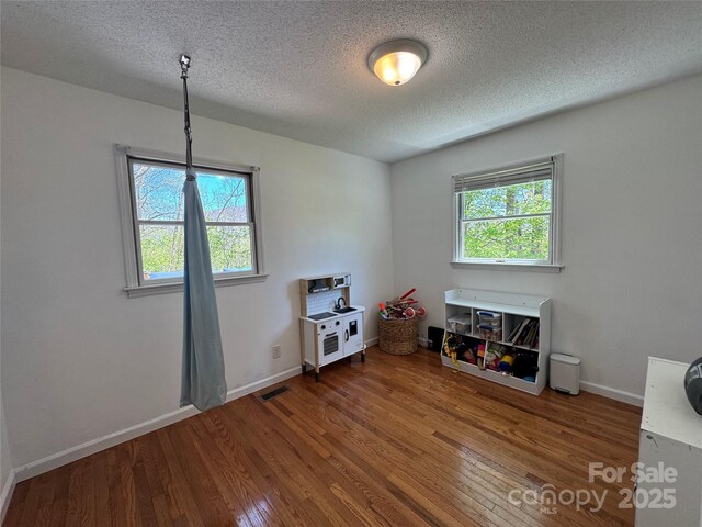 rec room featuring a textured ceiling, baseboards, visible vents, and wood finished floors