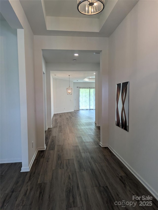 hallway featuring baseboards, a chandelier, dark wood-style floors, and a tray ceiling
