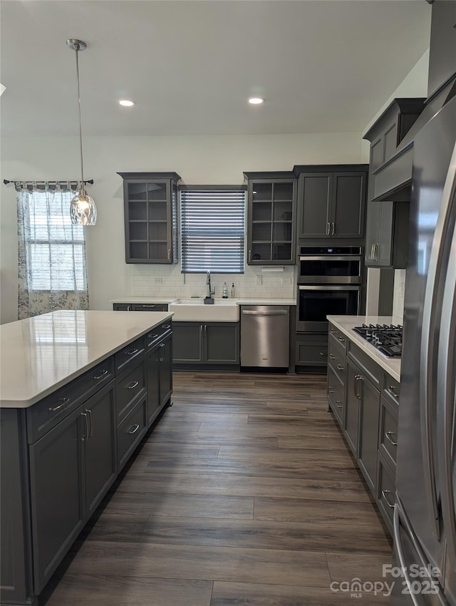 kitchen with appliances with stainless steel finishes, a sink, light countertops, tasteful backsplash, and glass insert cabinets