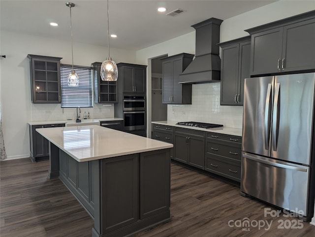 kitchen featuring glass insert cabinets, premium range hood, light countertops, a sink, and appliances with stainless steel finishes