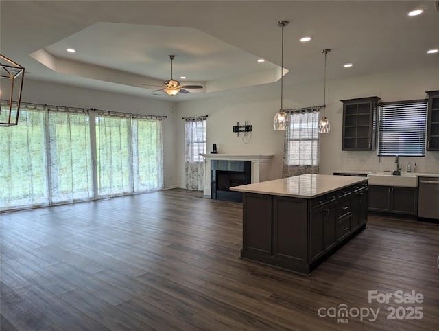 kitchen with a sink, a raised ceiling, dark wood finished floors, and light countertops